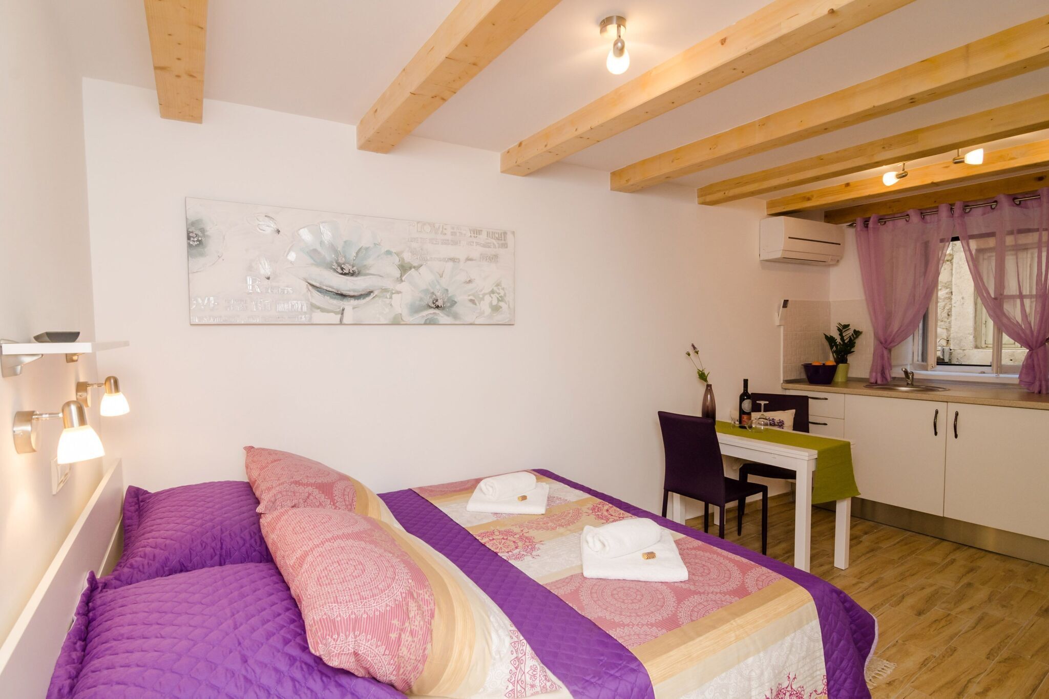 A bedroom with a bed, a desk, and a kitchenette.