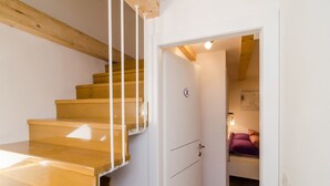 Eine Treppe mit Holzbodenstufen und weißen Wänden führt zu einem Zimmer mit einem Bett und einem kleinen Tisch.
