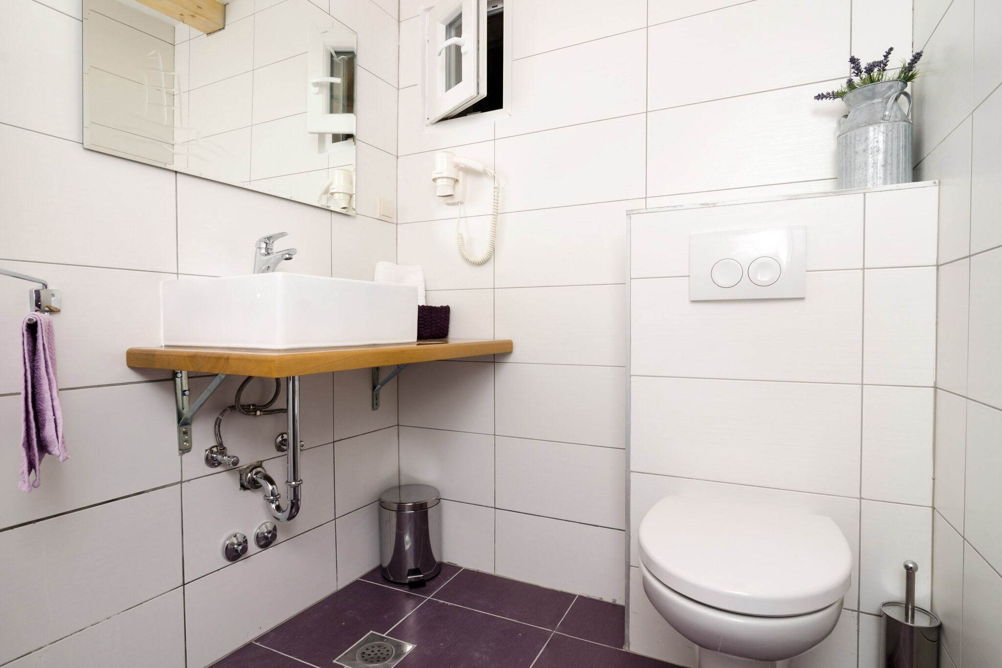 A bathroom with a white sink, a toilet, a mirror, a shower, and a trash can.