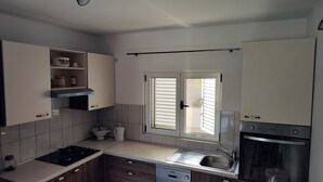 Une cuisine moderne équipée d’un four encastré, d’un lave-vaisselle et d’une fenêtre avec des stores.