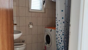 Une petite salle de bain comprenant des toilettes, un lave-linge et une fenêtre située au-dessus des toilettes.
