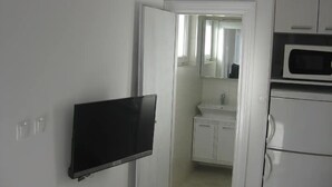 Cuina amb armaris blancs, microones i televisió de pantalla plana penjada a la paret.