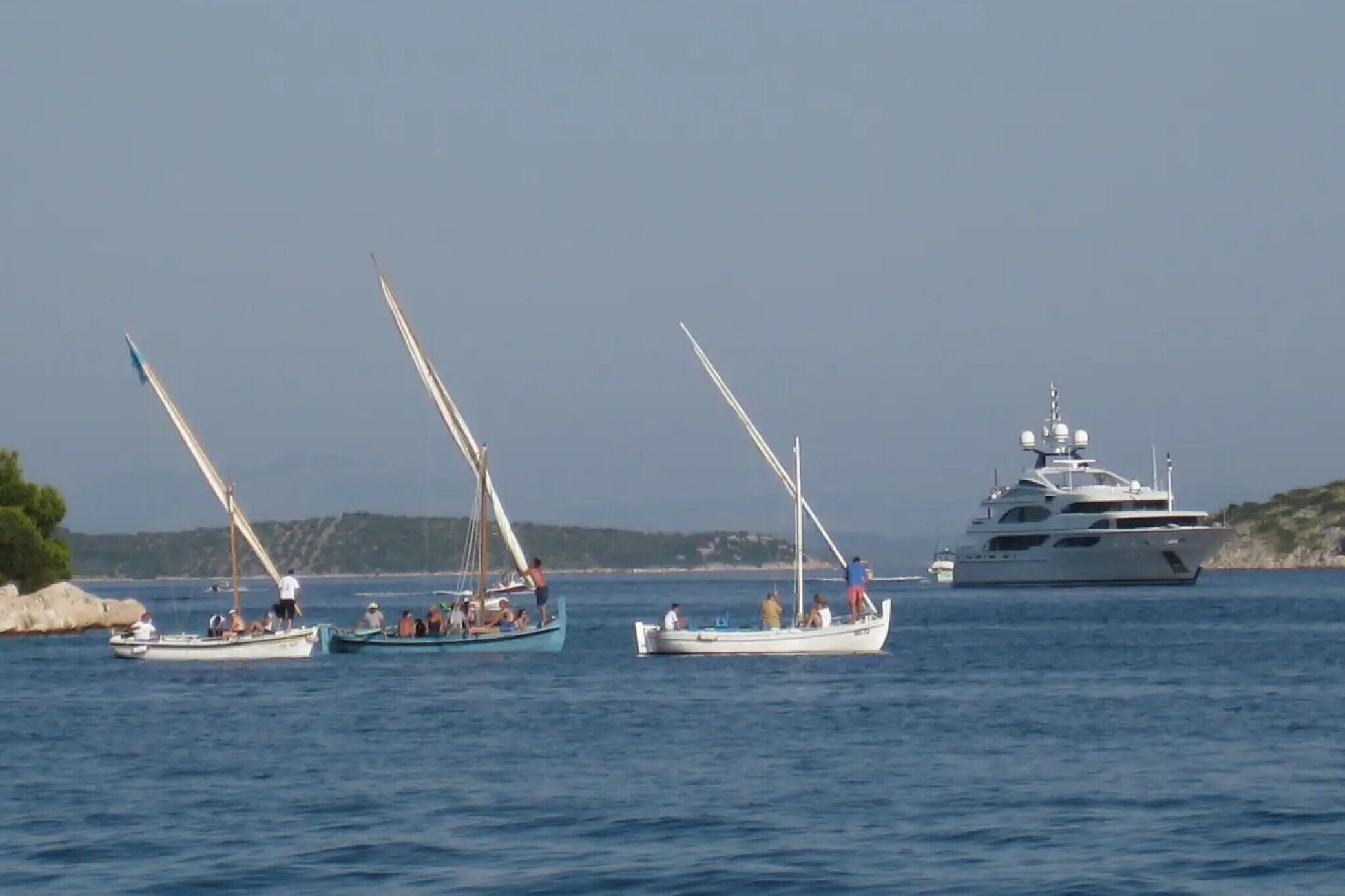 Trois voiliers sur une eau calme, avec un grand yacht en arrière-plan.