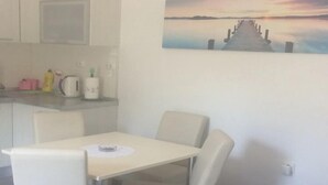 Una zona de dinar amb taula i caires, una cuina amb electrodomèstics, i un quadre d'un moll a la paret.