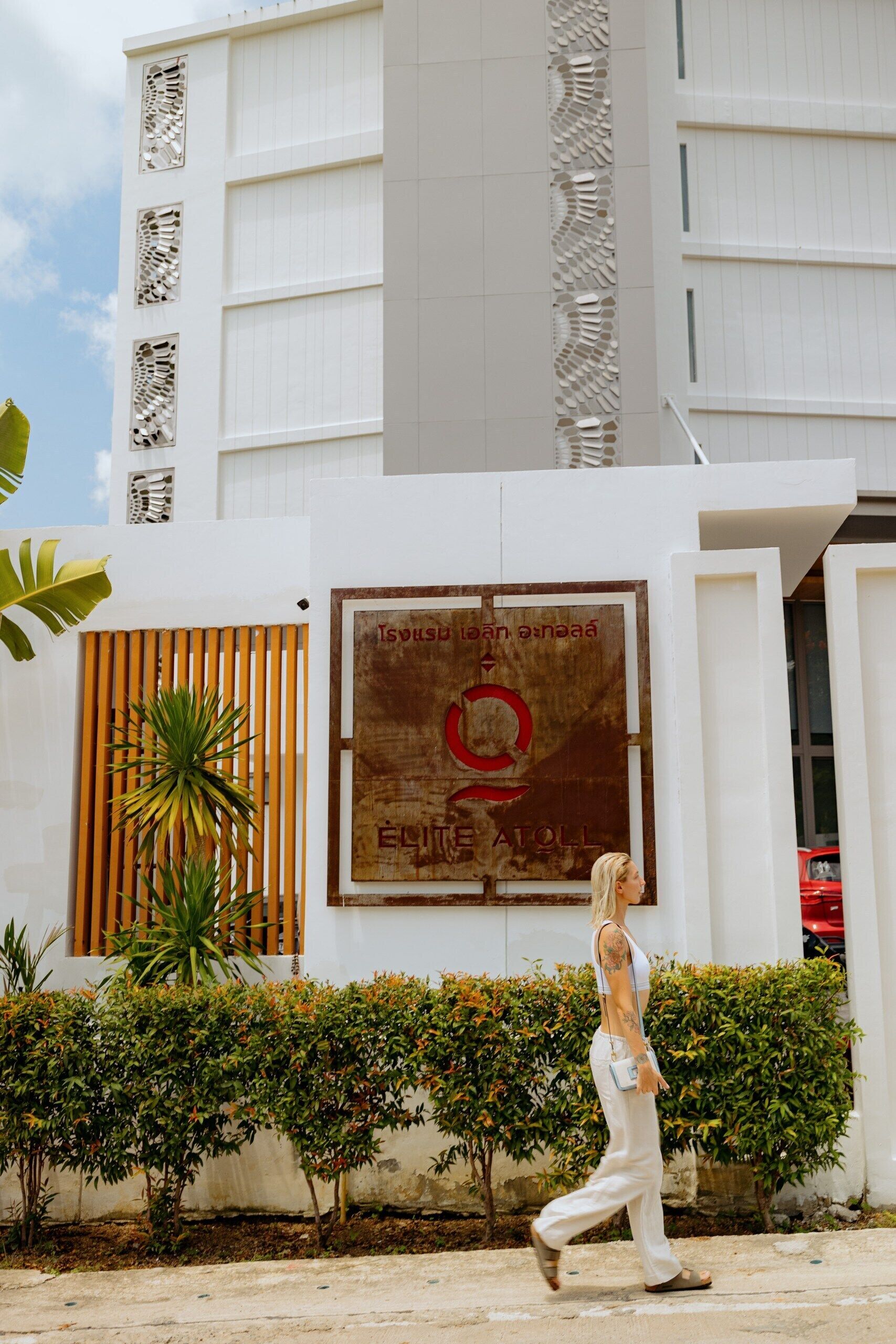 Ein modernes Gebäude mit einem großen Schild, auf dem "EQUITATE ATOLL" steht, und eine Person, die davor entlanggeht.