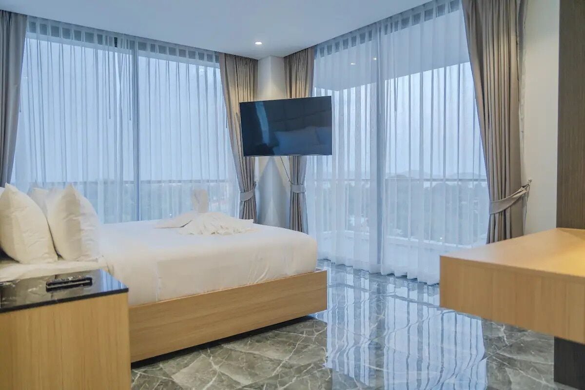 Ein modernes Hotelzimmer mit einem großen Bett, einem an der Wand montierten Flachbildfernseher und einem Balkon mit Vorhängen.