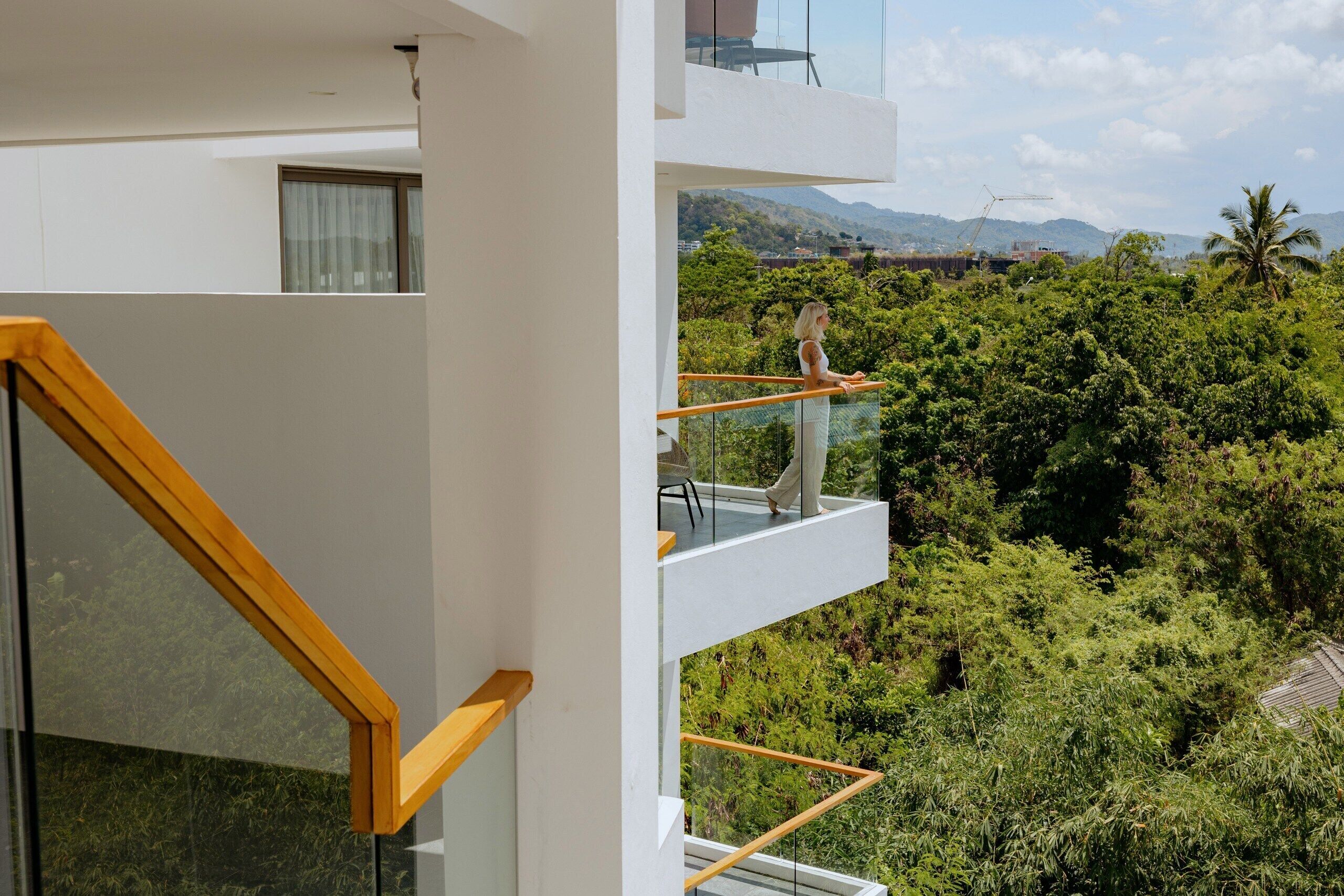 A modern building with a balcony overlooking a lush green landscape and distant mountains.