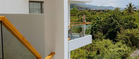 A modern building with a balcony overlooking a lush green landscape and distant mountains.