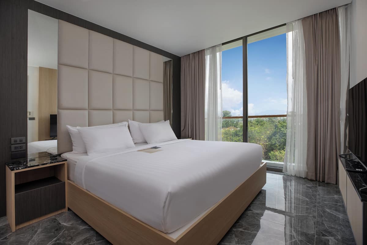 Une chambre d’hôtel moderne, dotée d’un grand lit, d’une table de chevet, d’une télévision et offrant une vue sur l’extérieur.