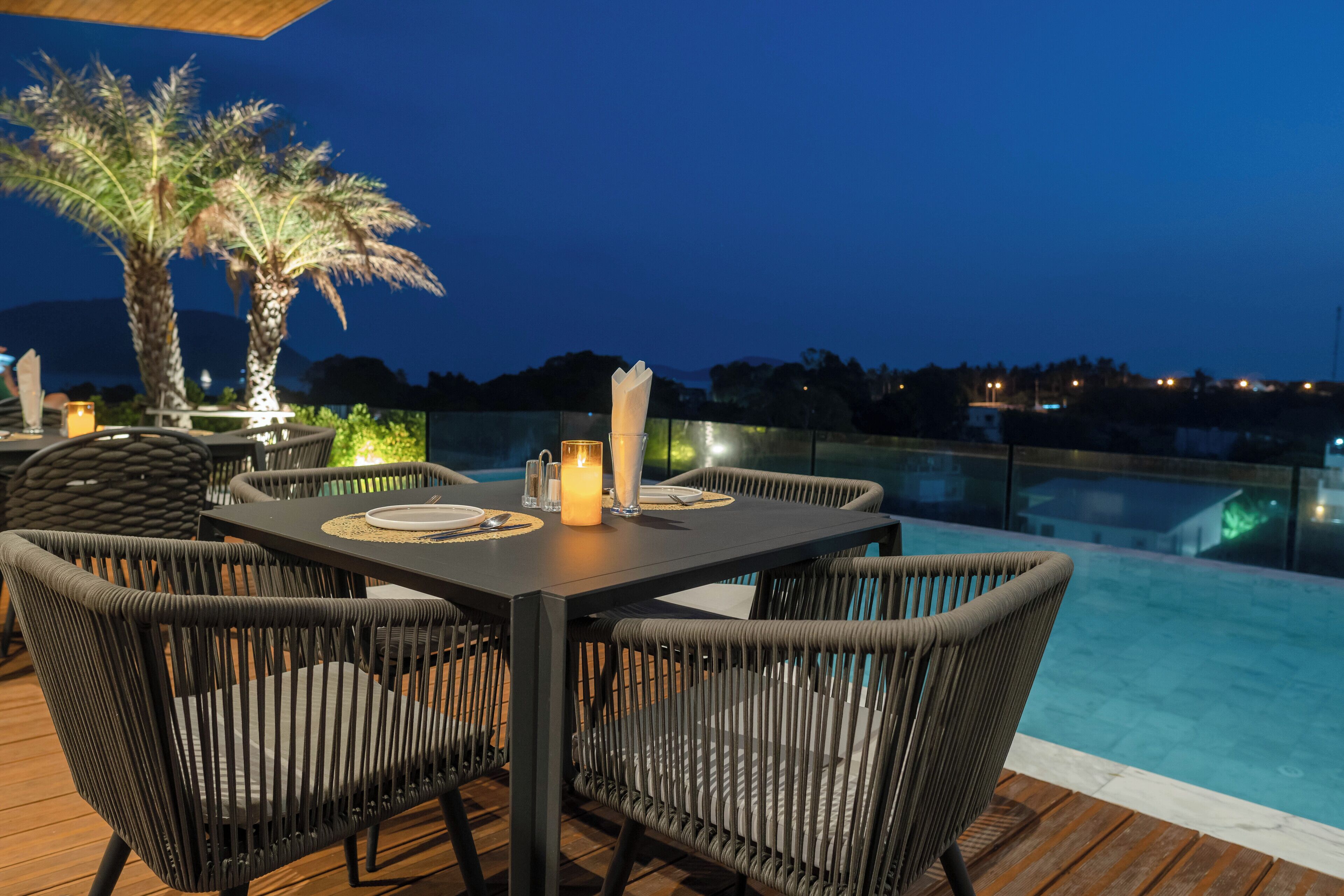 An outdoor dining area with wicker chairs and a table set for two, overlooking a pool.