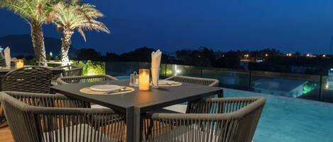An outdoor dining area with wicker chairs and a table set for two, overlooking a pool.