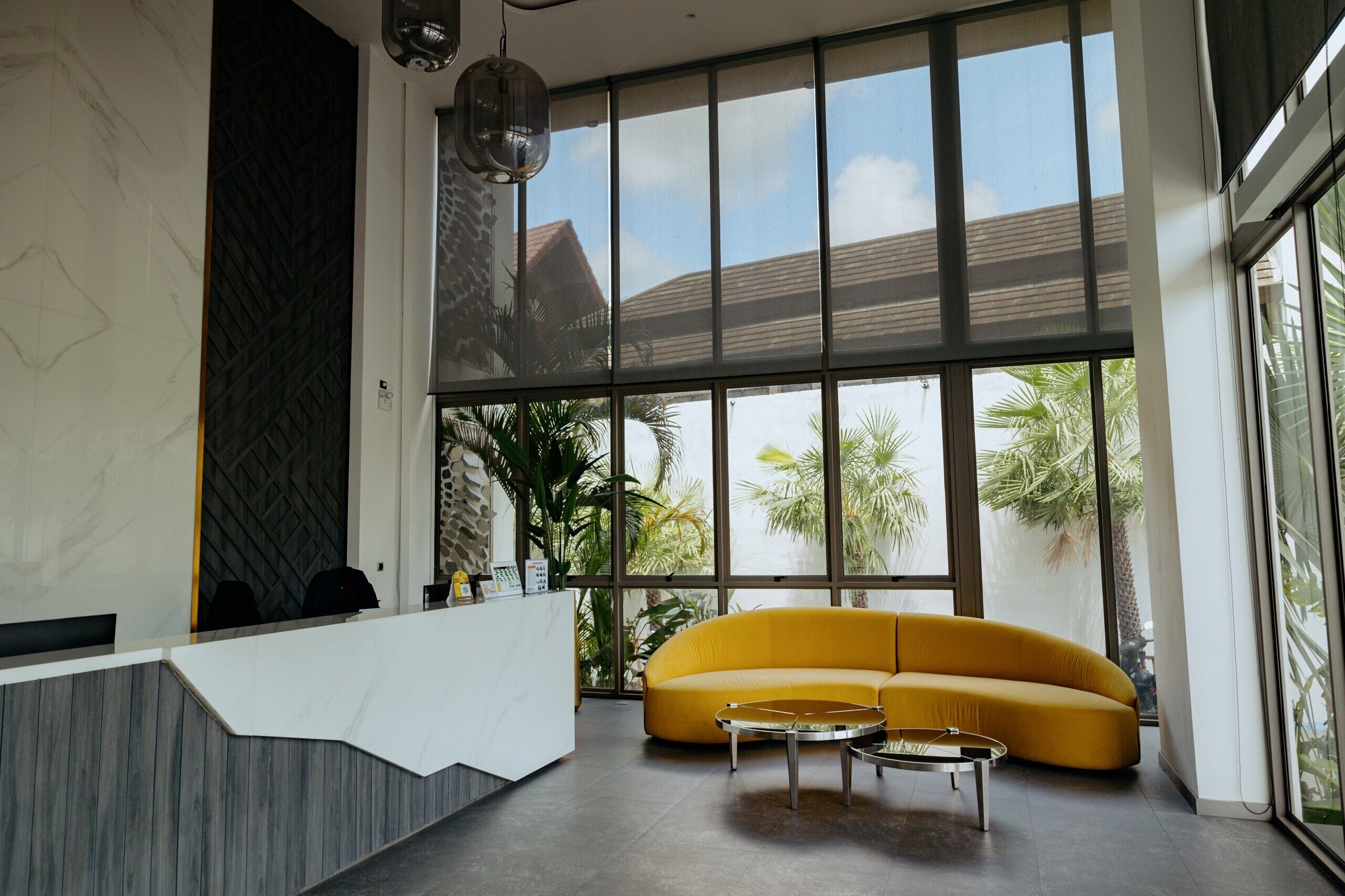 Un área de recepción con un mostrador blanco, un sofá amarillo y una mesa de centro redonda.