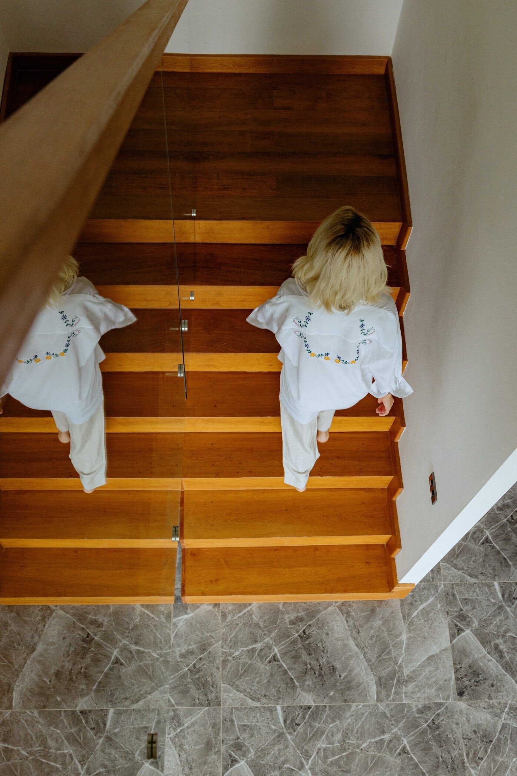 A wooden staircase with a glass railing, leading to a room with a tiled floor.