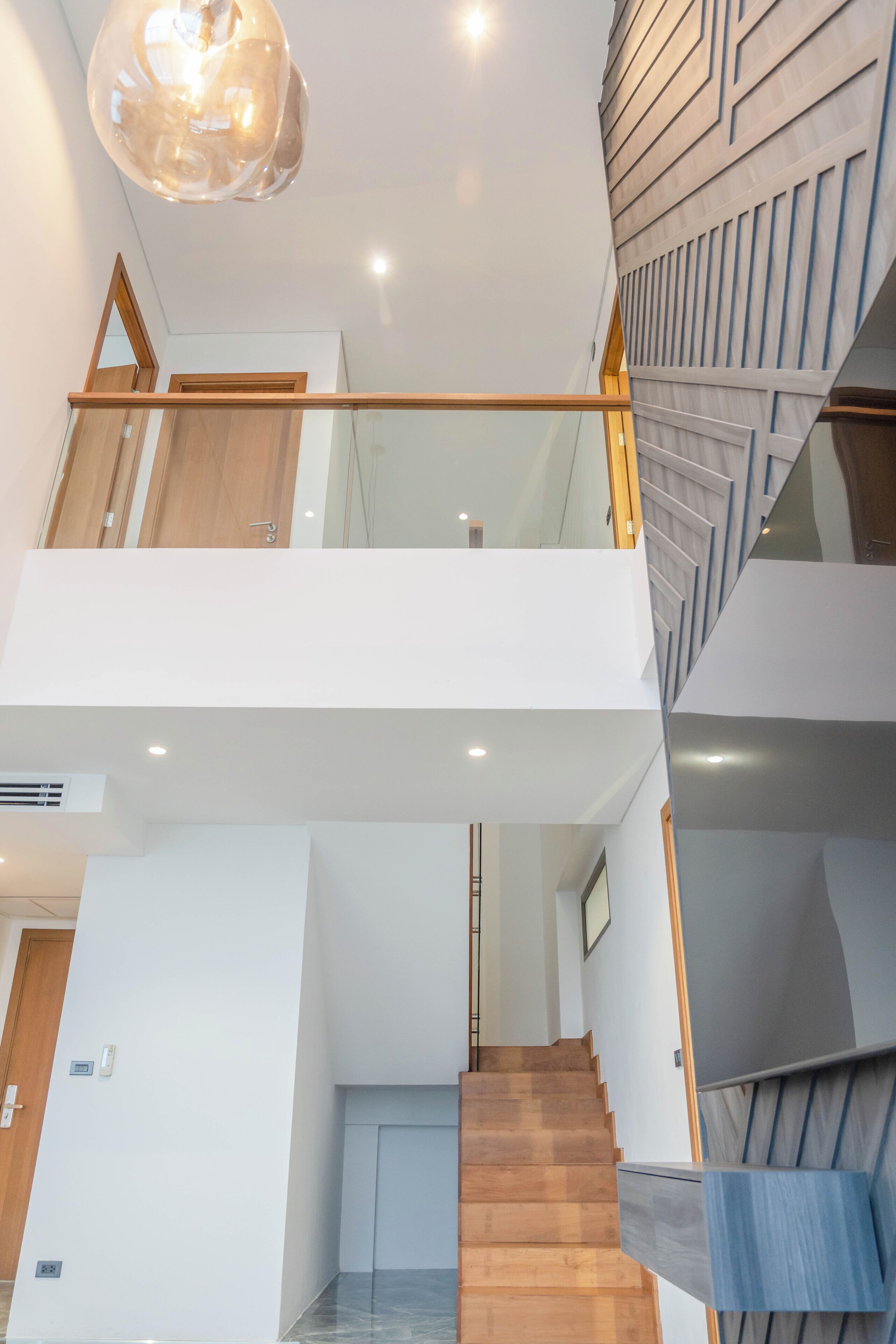 A modern interior with a wooden staircase, glass railings, and a decorative wall panel.