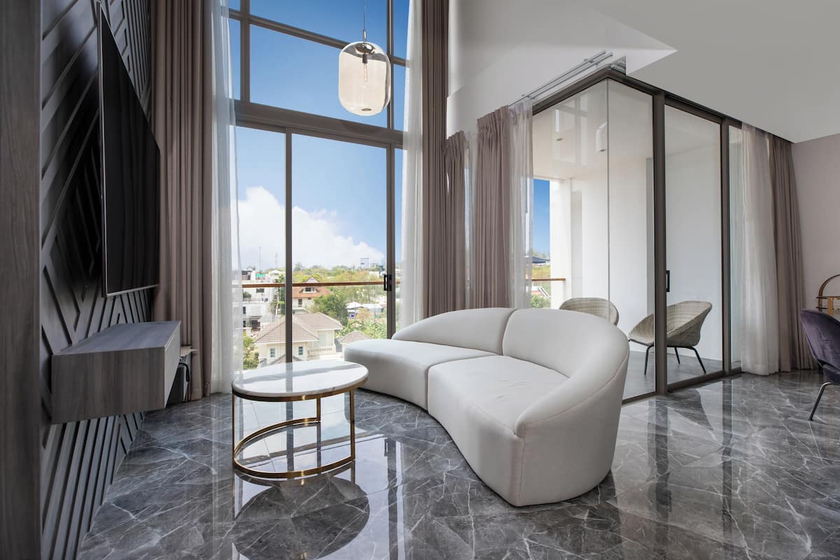 Un salon moderne avec un canapé blanc aux lignes courbes, une table basse ronde en verre et une vue sur la ville grâce à de grandes fenêtres.