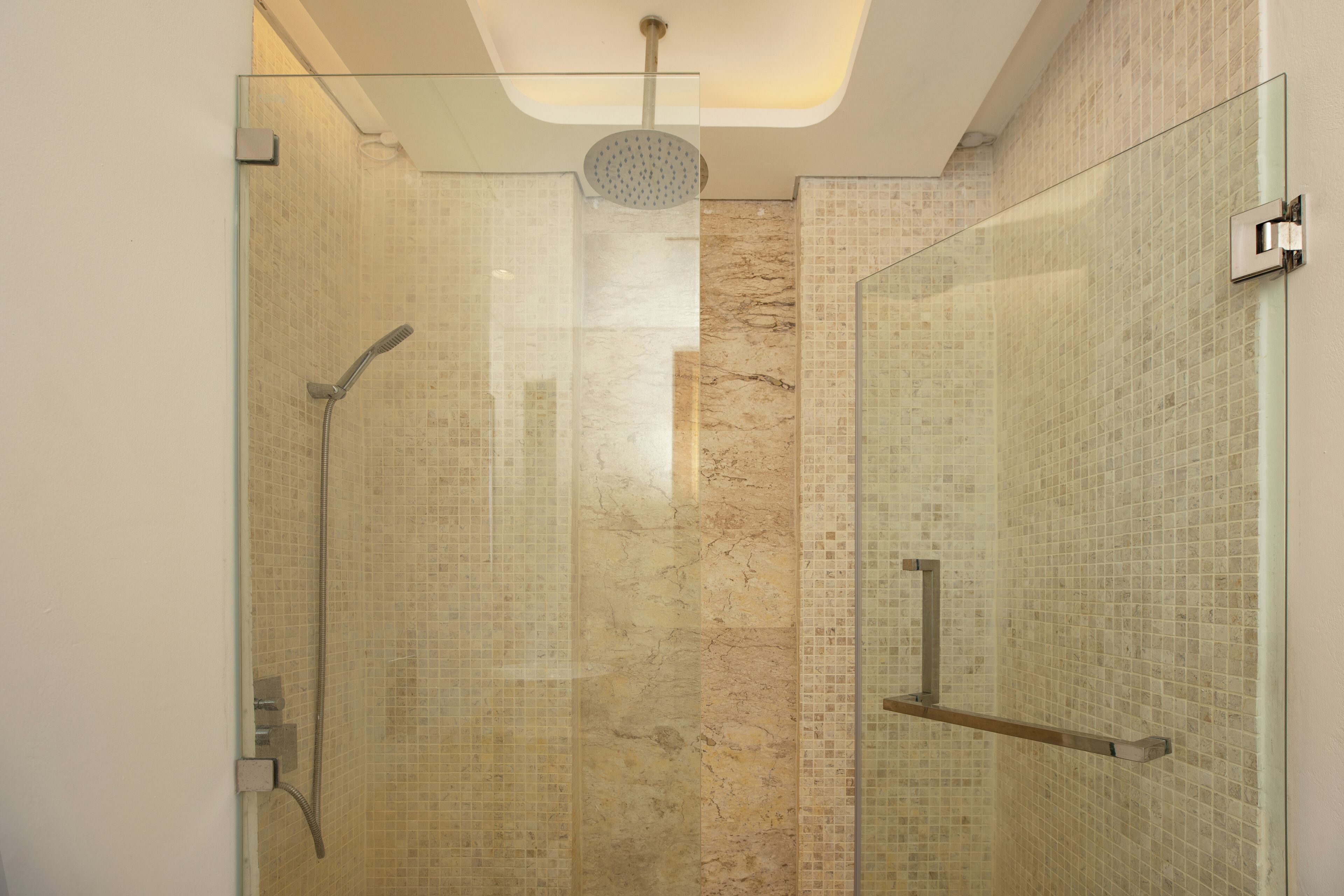 Een douche met glazen wanden, een handdouche en een wandmengkraan.