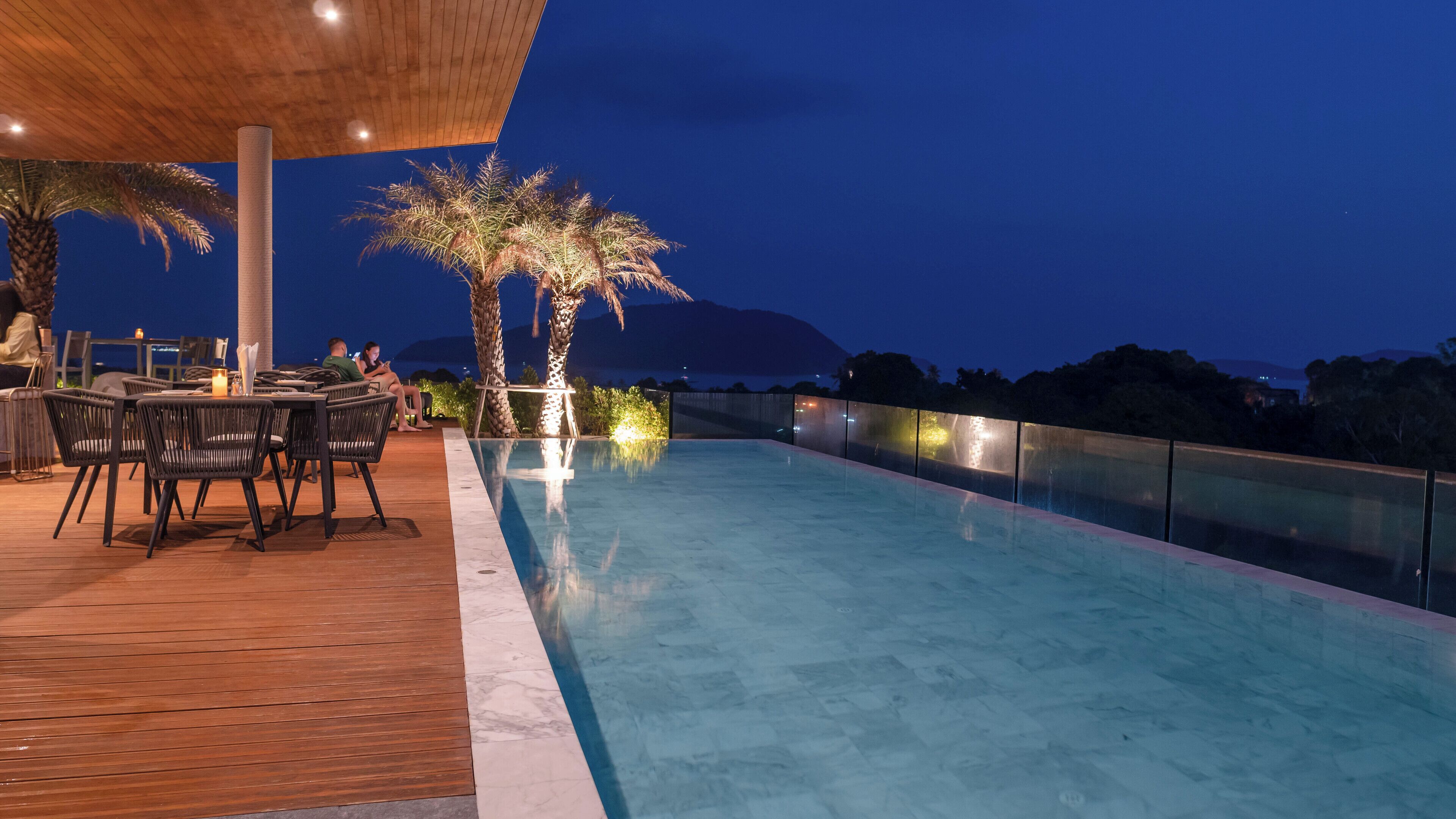 Un espace piscine extérieur doté d’une terrasse en bois, de sièges et de palmiers.