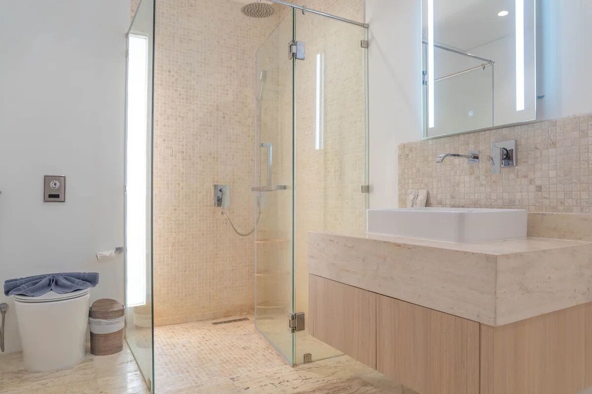 A modern bathroom with a glass-enclosed shower, a large mirror, and a marble countertop.