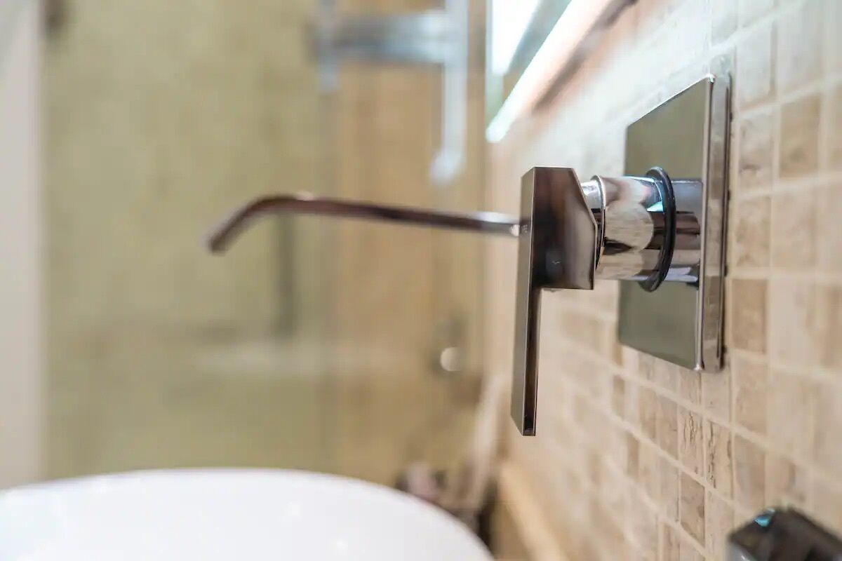 A bathroom with a tiled wall, a sink, and a faucet with a lever handle.