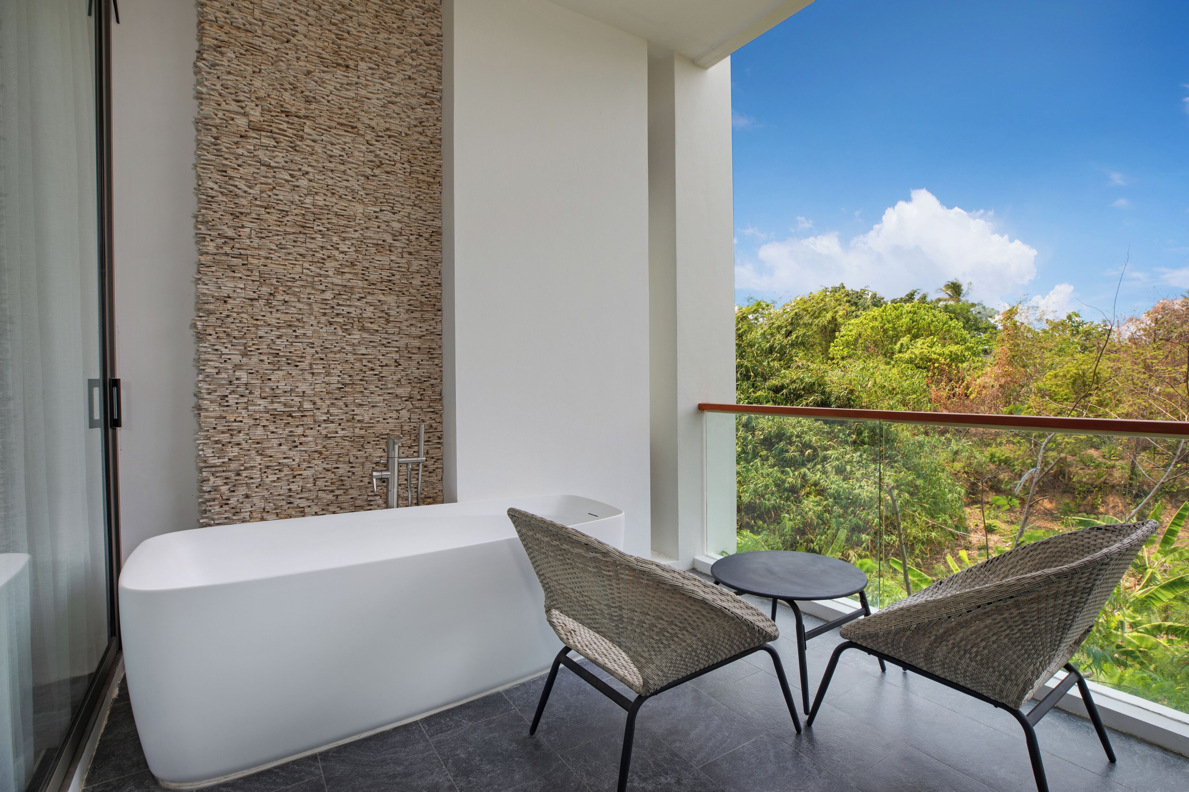 Un bagno moderno con una vasca da bagno bianca, una parete in pietra e un balcone con sedie in vimini e un tavolo.