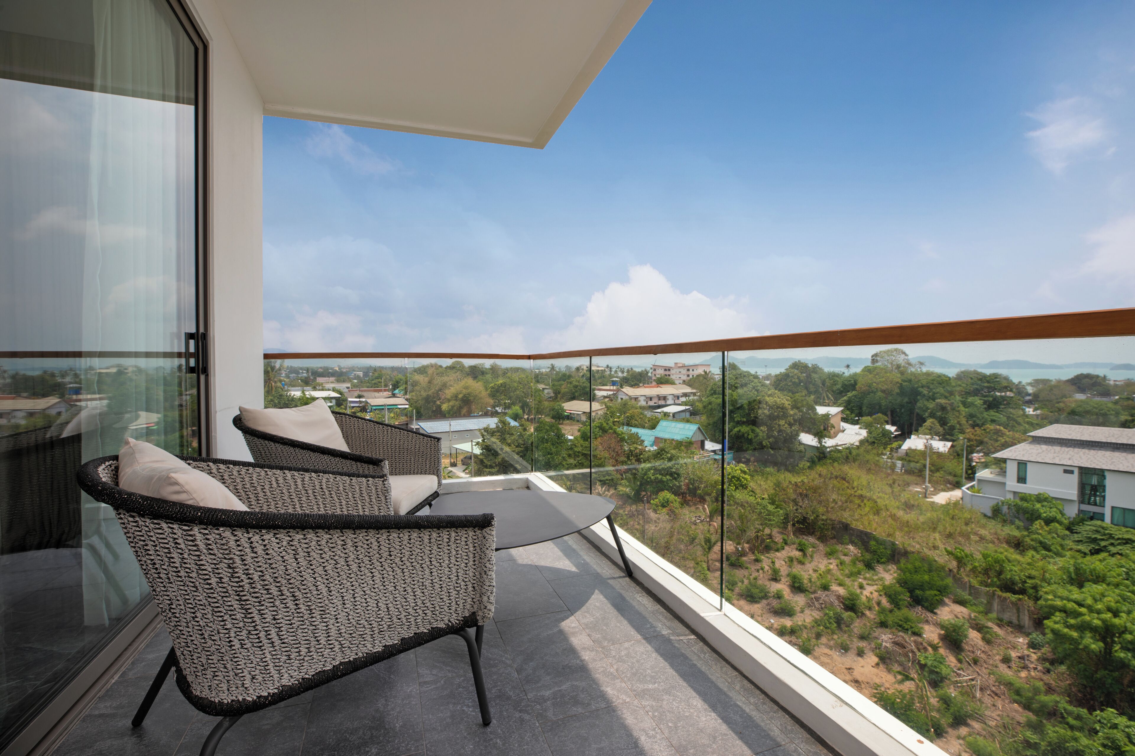 A balcony with wicker furniture and a glass railing overlooking a residential area.