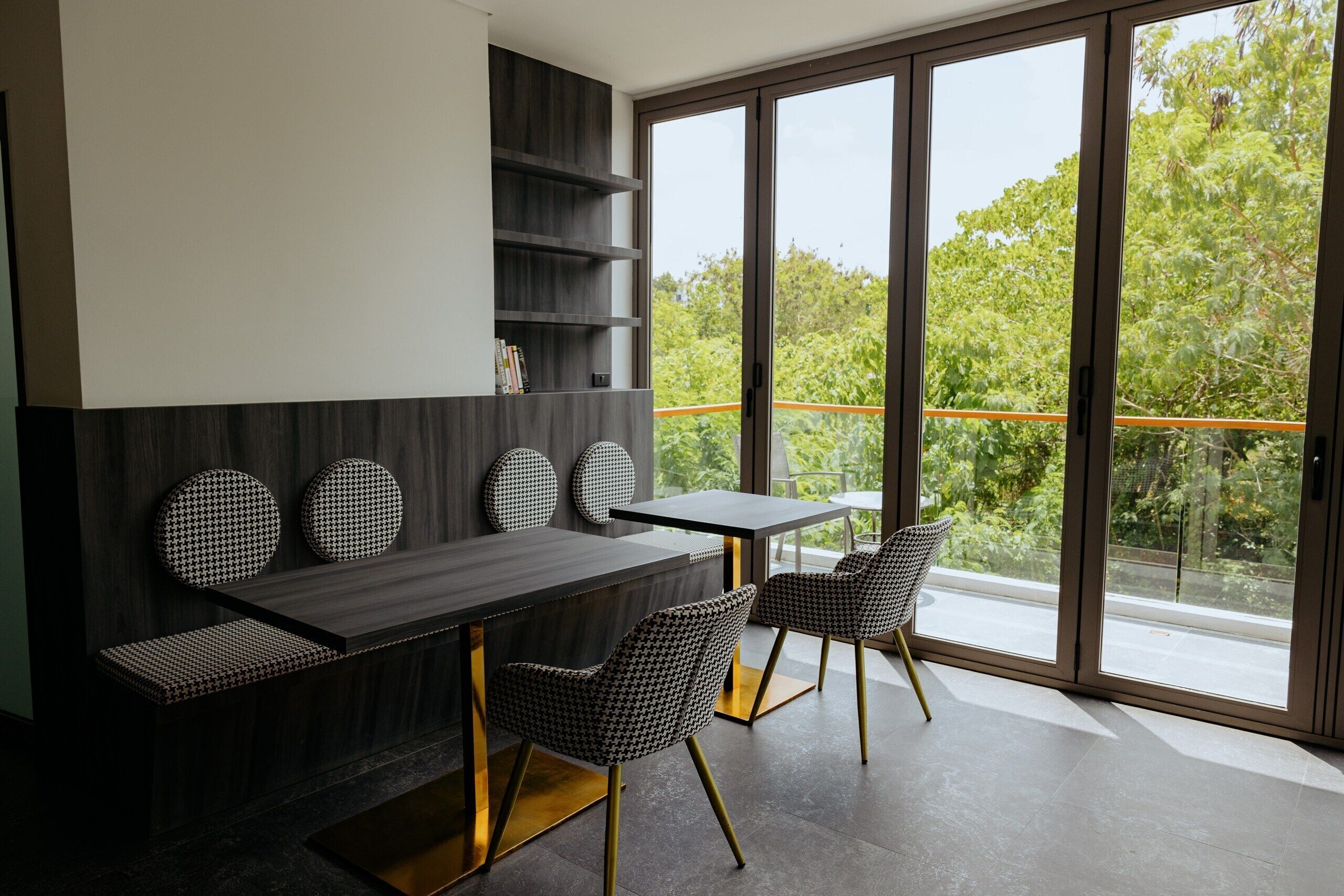 A modern dining area with a dark wood table, two chairs, and a bench. There are shelves with books and decorative items.