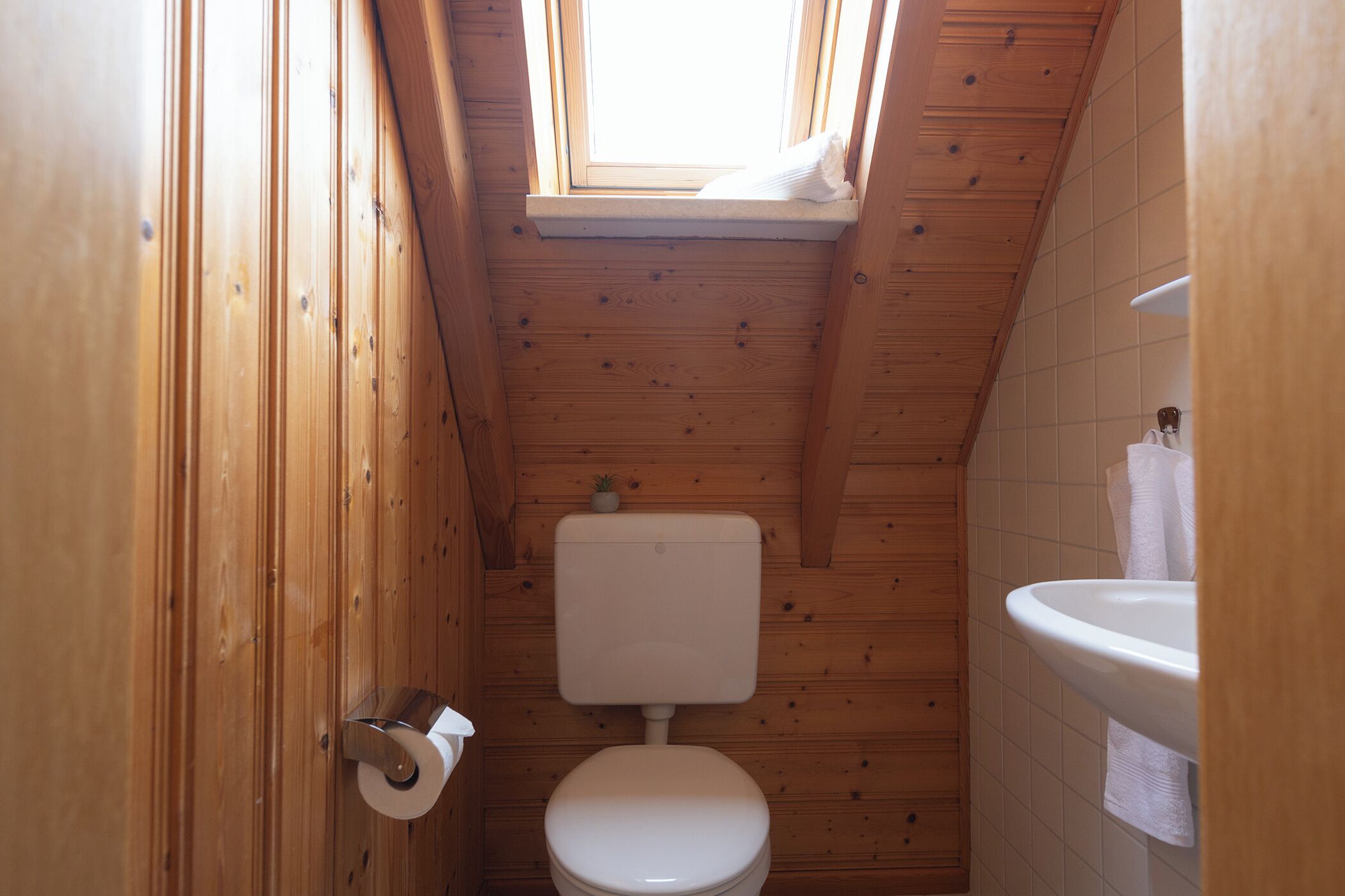 Ein kleines Badezimmer mit Holzvertäfelung, Toilette, Waschbecken und einem Oberlicht.
