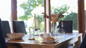 A dining table with a basket, a glass, a cup, a vase with flowers, and a pastry. - Vacation home Lichtes Haus am Feld. With two terraces and close to the coast. (Wurster Nordseeküste)