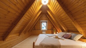 A cozy attic bedroom with wooden beams, a bed, a window, and a bedside table. - Vacation home Lichtes Haus am Feld. With two terraces and close to the coast. (Wurster Nordseeküste)