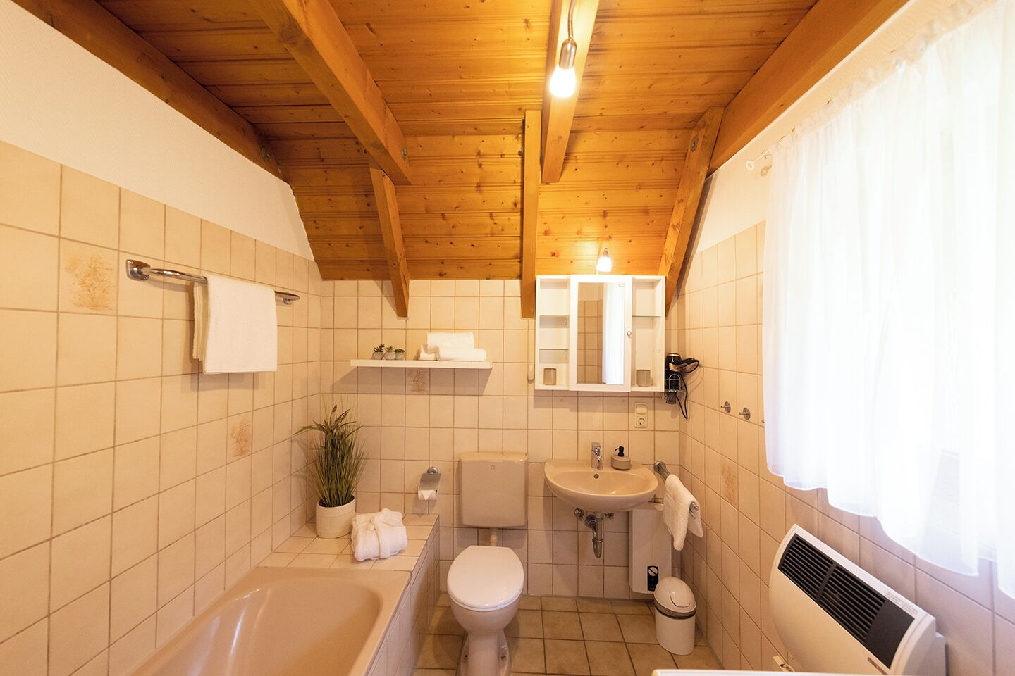 A bathroom with a wooden ceiling, a bathtub, a toilet, a sink, and a mirror.