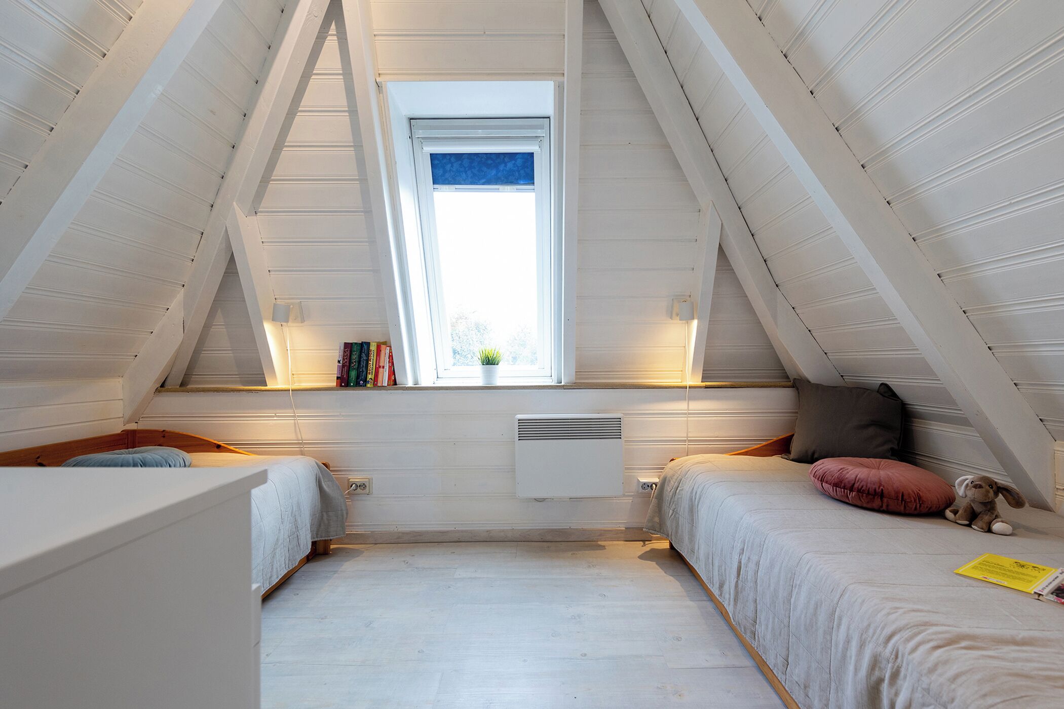 Een knus slaapkamer op zolder met twee bedden, een raam en een radiator.