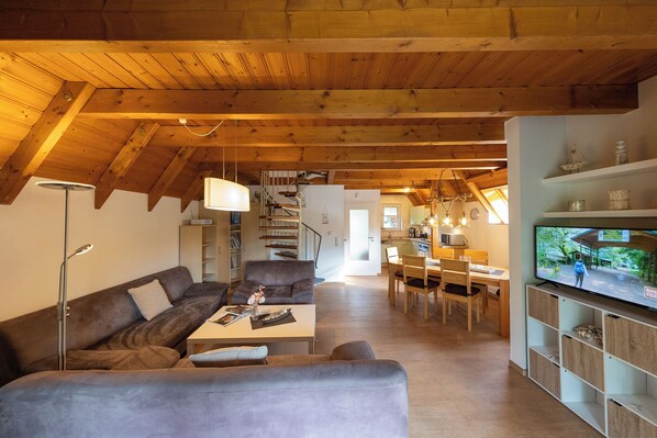 Een ruime woonkamer met een hoog houten plafond, een bank, een salontafel en een televisie.