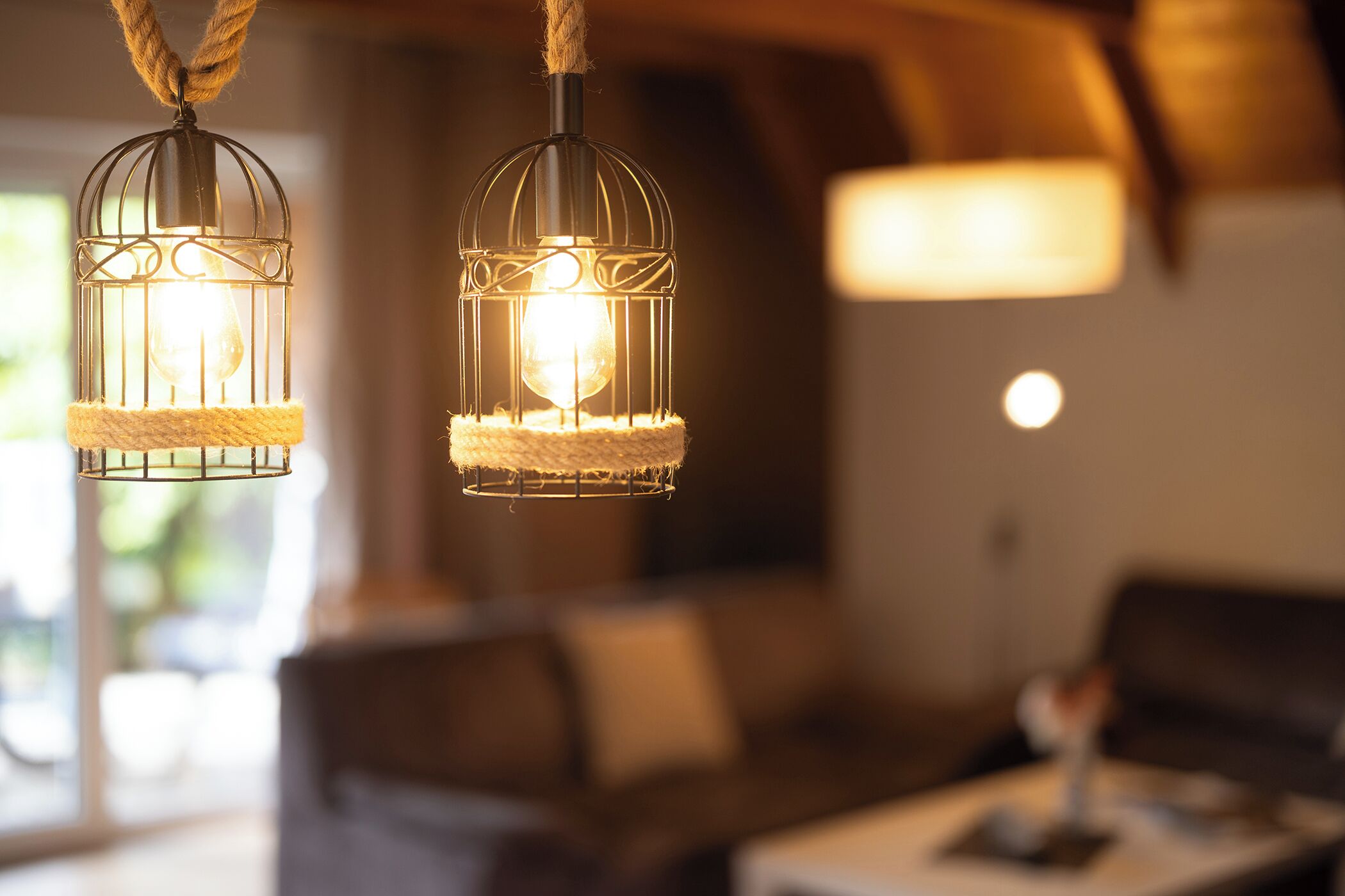 Dos lámparas colgantes con una luz cálida, un sofá y una mesa en un ambiente acogedor.