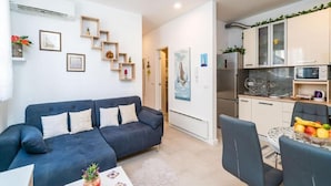 Een moderne woonkamer met een donkerblauwe bank, een eettafel met stoelen, en een keuken met witte kasten en een koelkast.