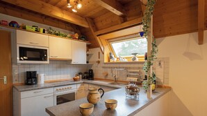 A kitchen with white cabinets, a microwave, a stove, and a window with a view of greenery. - Vacation home Medemsand 1, idyllic and in the middle of the action. (Wurster Nordseeküste)