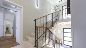 Eine Treppe mit hölzernem Geländer und schwarzen Metallspindeln, die zu einer oberen Etage führt.