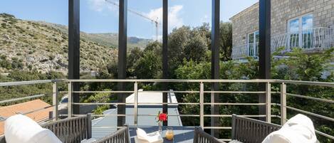 A balcony with wicker furniture, a table with a book and a glass of orange juice, and a view of a construction site and a building with a balcony.