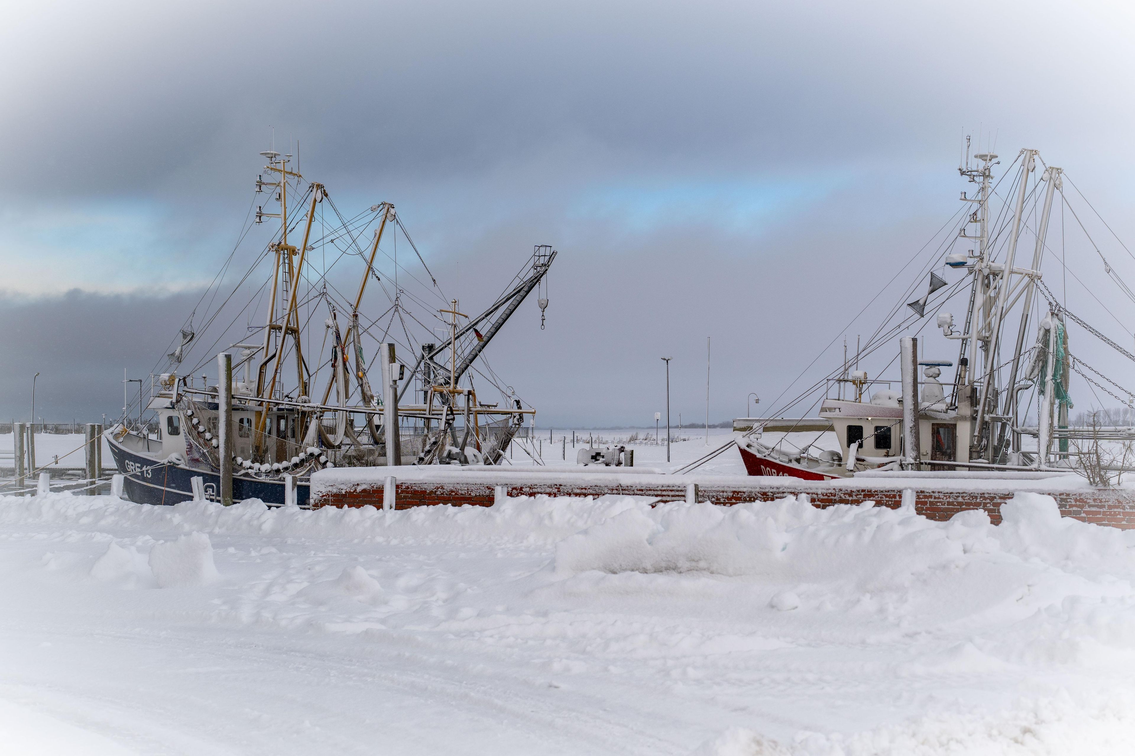 A harbor with two boats docked, surrounded by snow.