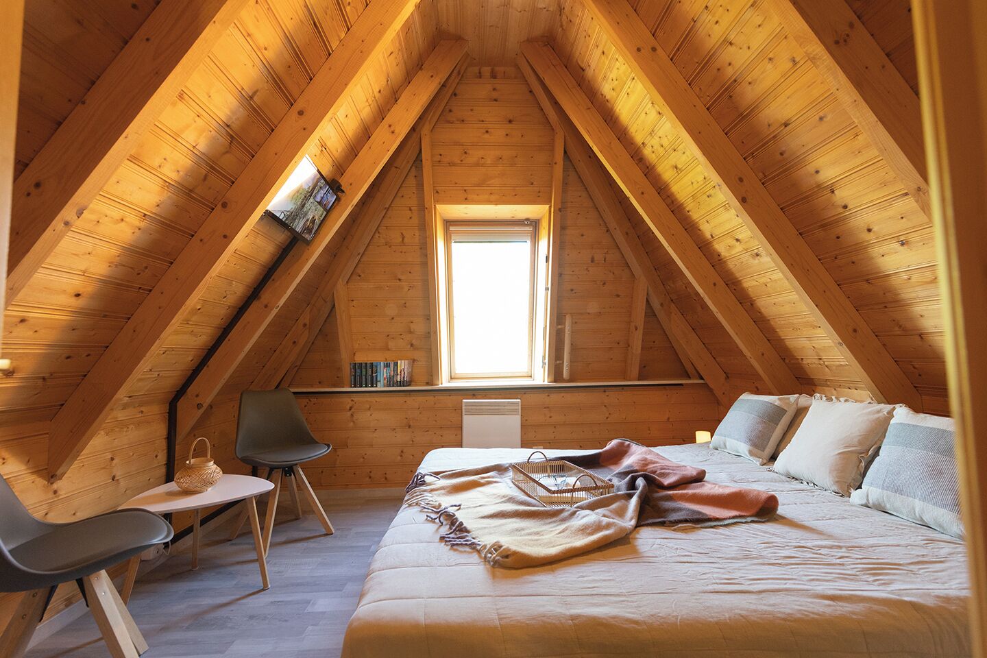 Ein gemütliches Schlafzimmer im Dachgeschoss mit schrägverdeckter Decke, einem Bett, einem Schreibtisch und einem Stuhl.
