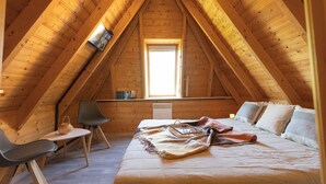 A cozy attic bedroom with a sloped ceiling, a bed, a desk, and a chair.