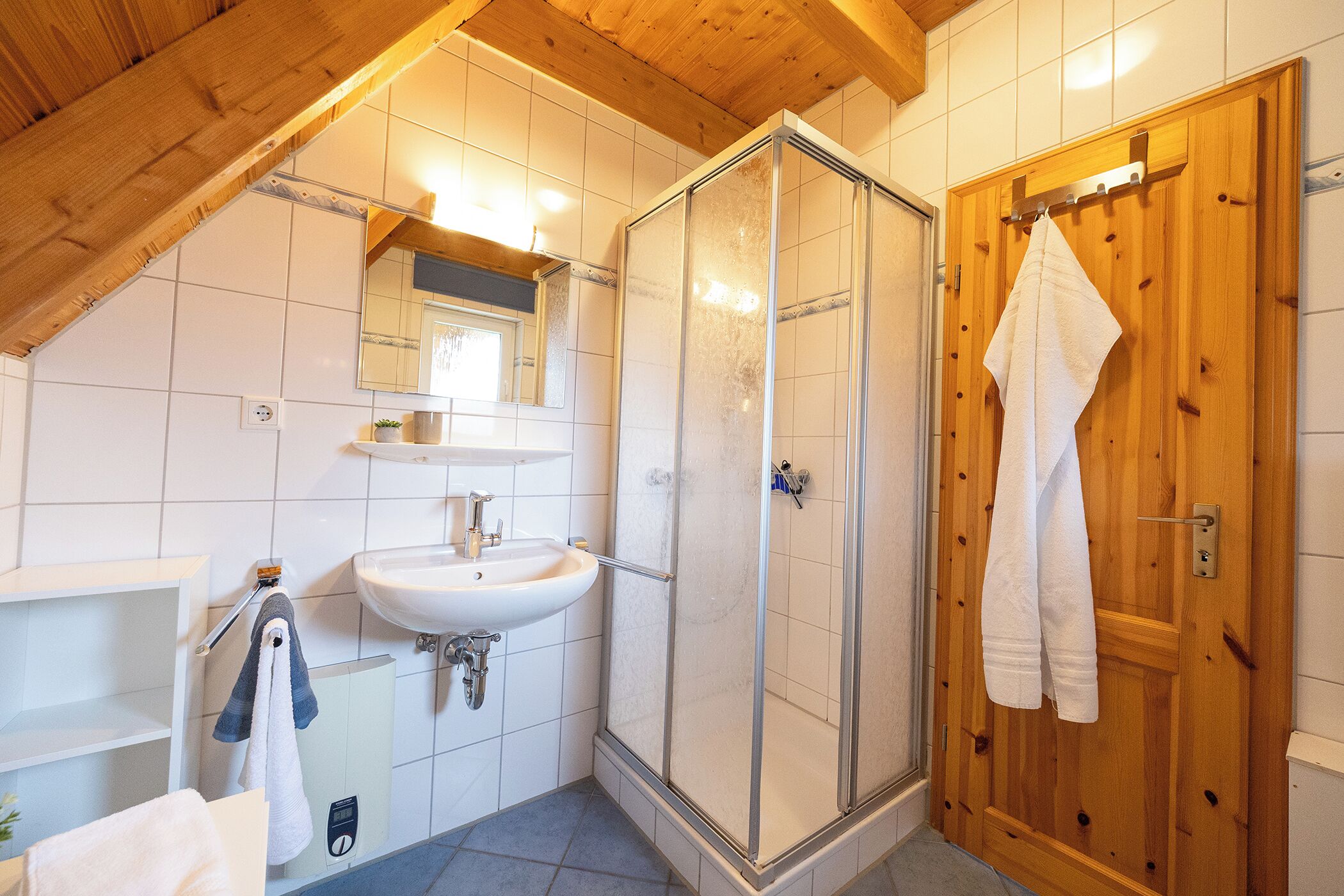 Un baño con techo de madera, cabina de ducha de vidrio, lavamanos y una toalla colgada en un gancho.
