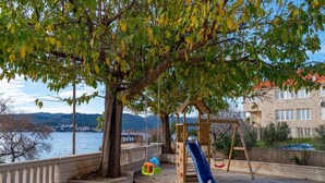A playground with a slide and climbing wall, located near a waterfront with a stone building in the background. - Villa Ponar with Swimming Pool (Kuciste)