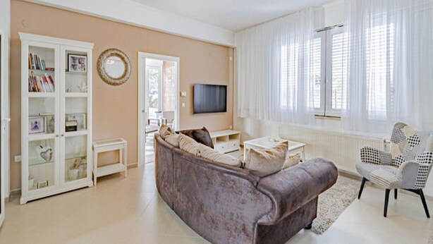 Un salon avec un canapé beige, un meuble blanc, un téléviseur et une fenêtre ornée de rideaux légers.
