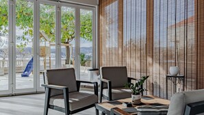 A modern indoor space with large sliding glass doors leading to an outdoor area. Inside, there are two armchairs, a wooden table with a plant, and a small side table with a white bowl. - Villa Ponar with Swimming Pool (Kuciste)