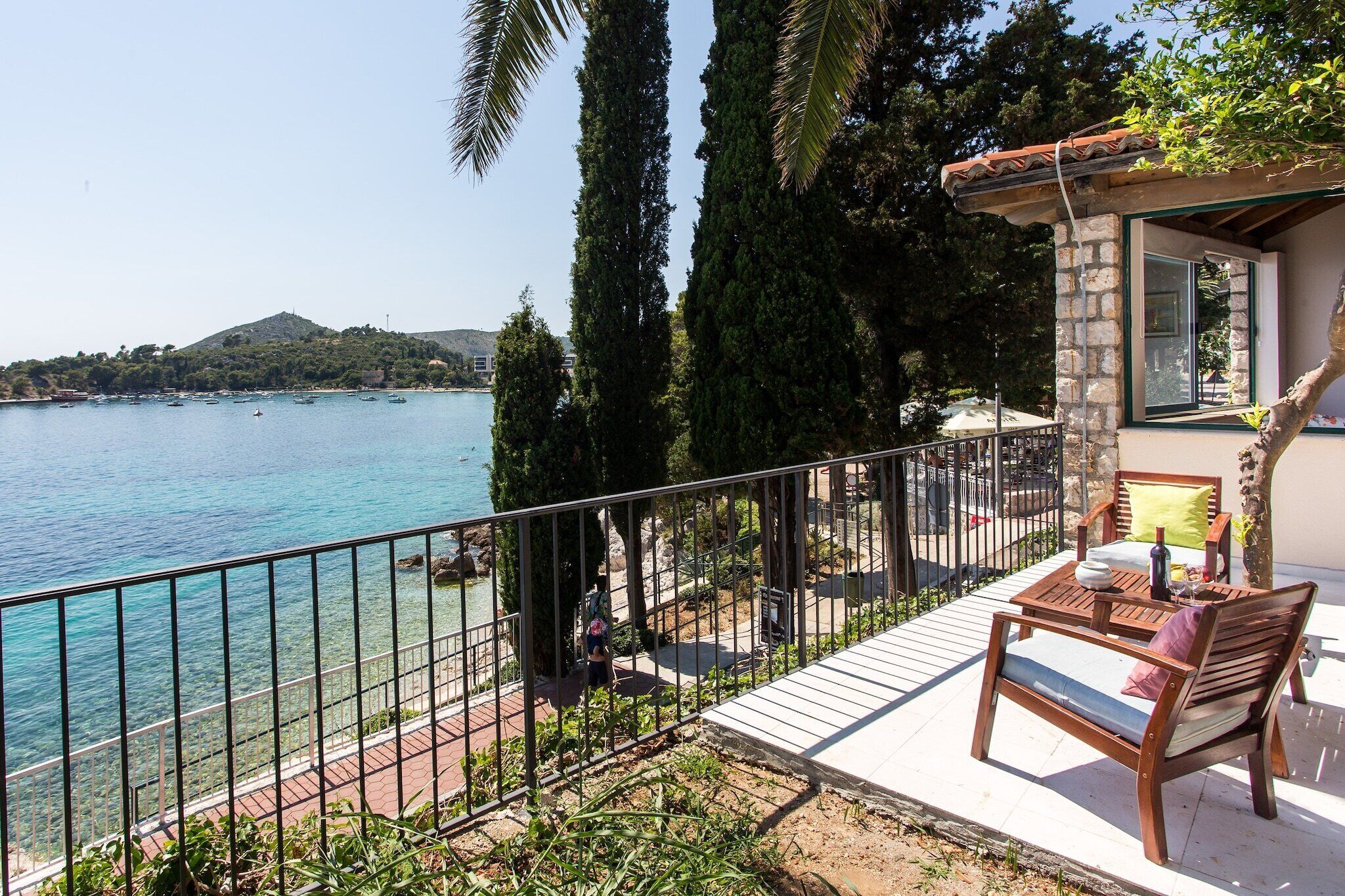 Un balcon donnant sur la mer, un banc en bois et un mur de pierre.