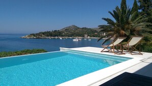 Ein Pool mit Blick auf das Meer und ein Berg. Zwei Liegestühle sind vorhanden.