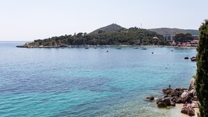 Küstensicht mit klarem Wasser, einer kleinen Insel mit Gebäuden und felsiger Küstenlinie.