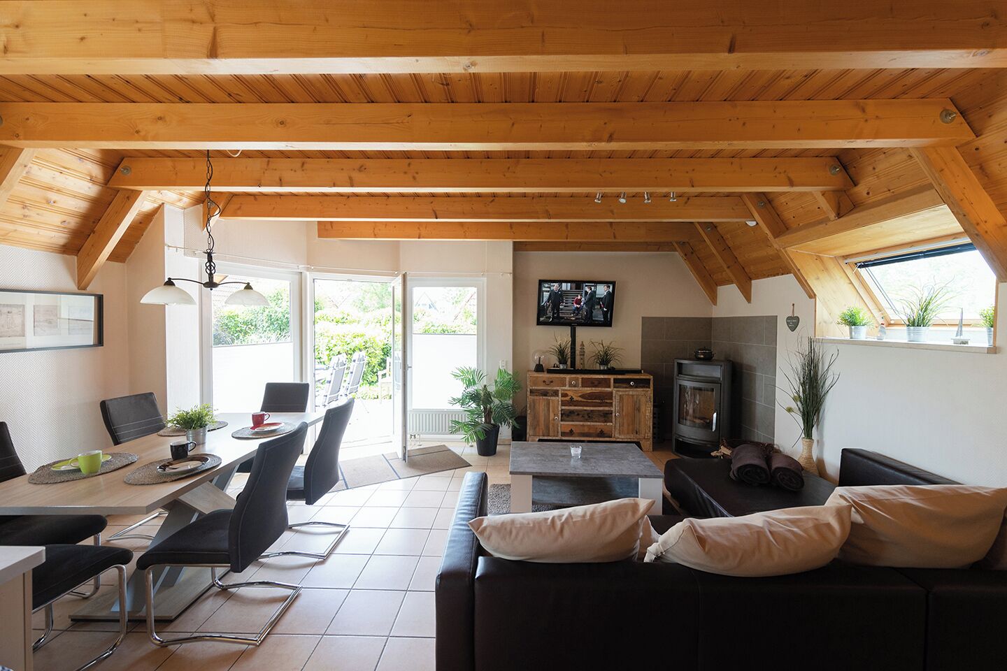 Una sala de estar acogedora con techo de madera, chimenea, televisor y comedor con sillas y mesa.
