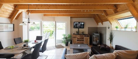 Una sala de estar acogedora con techo de madera, chimenea, televisor y comedor con sillas y mesa.