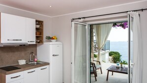 A compact kitchen with a sink, cabinets, and a refrigerator. A sliding glass door leads to a balcony with a table and chairs, overlooking the sea. - Villa Mirjana - Studio Apartment with Terrace and Sea View (Bogumila) (Mlini)